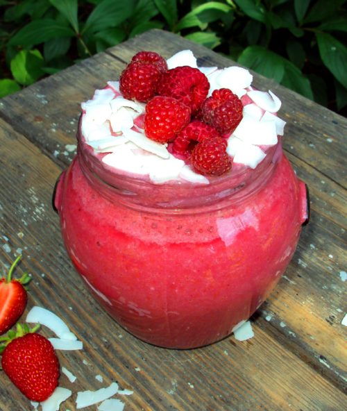 Raspberry Coconut Protein Mousse in a glass jar with frozen raspberries and coconut on a top
